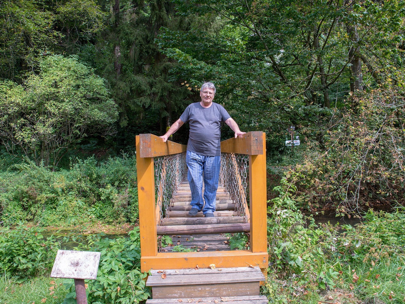 ein Mann geht über eine (mit Absicht wackelig gemachte) Holzbrücke