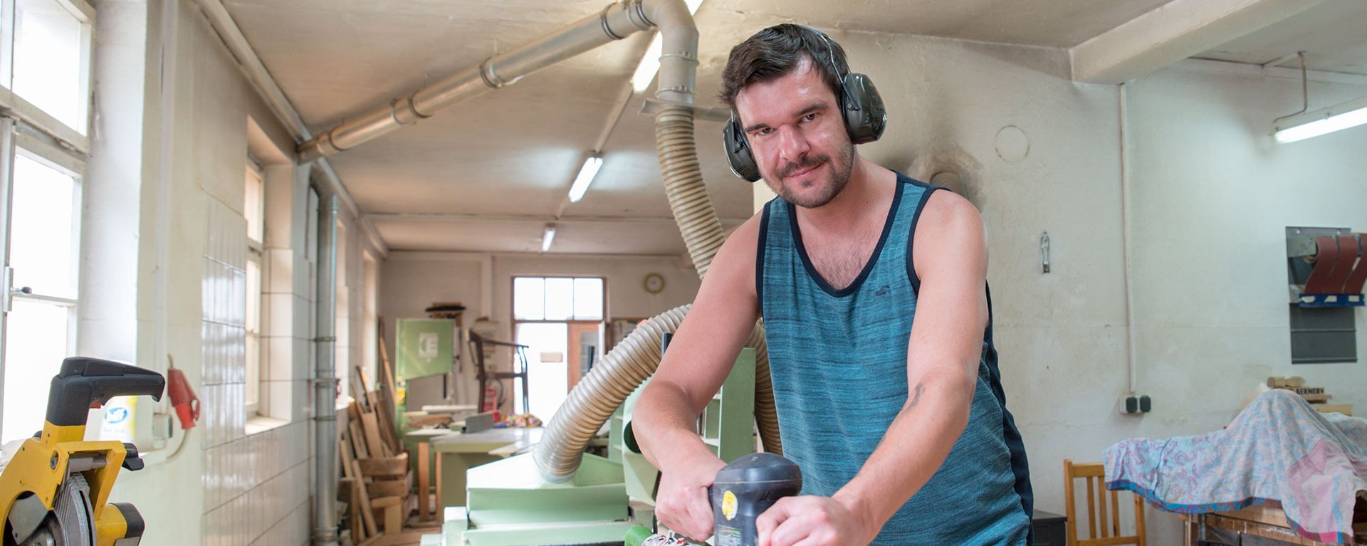 Holzwerkstatt: Ein Mann mit Gehörschutz arbeitet mit der Schleifmaschine