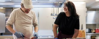 Zwei lachende Menschen arbeiten gemeinsam in der Küche.