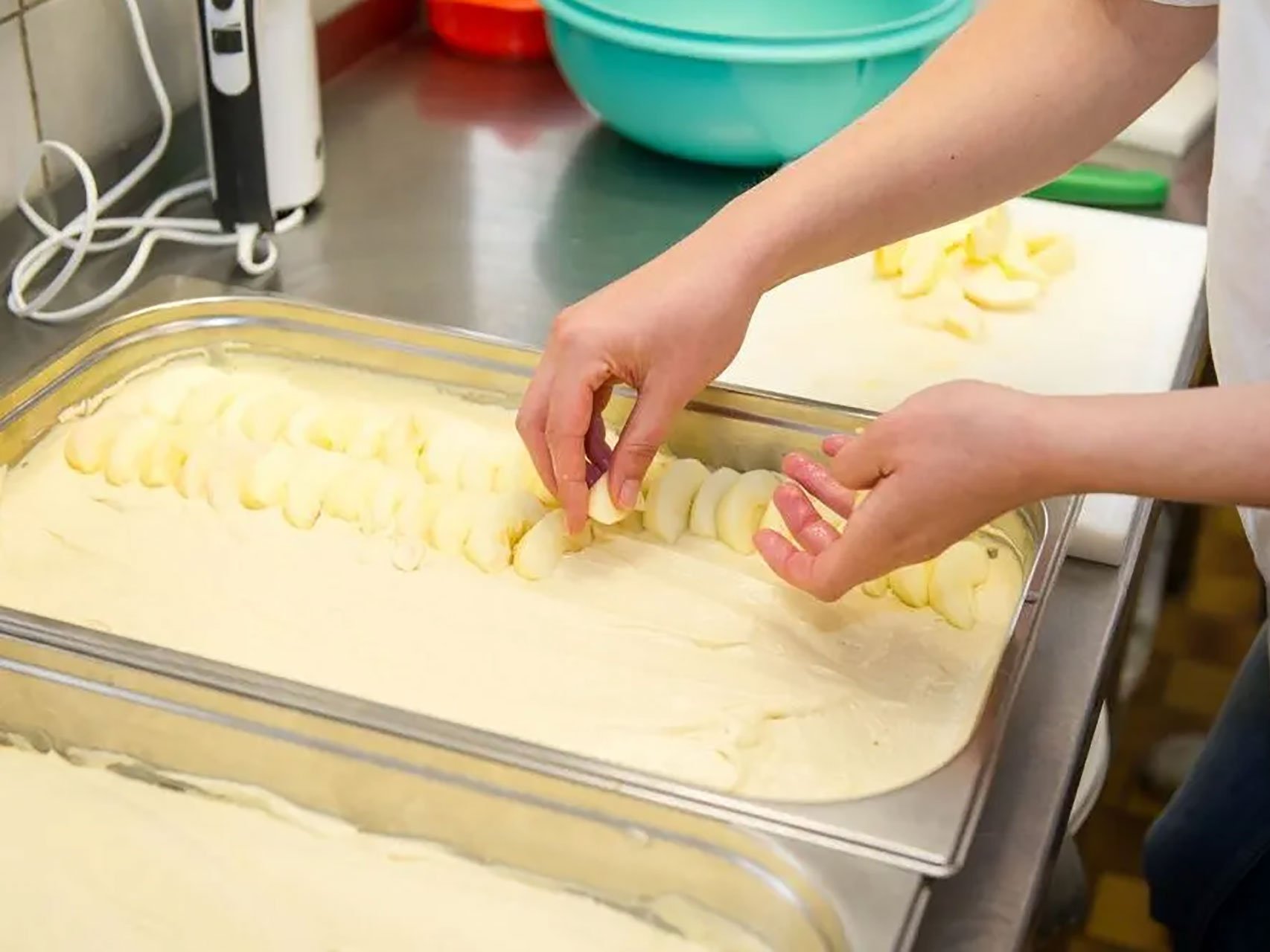 Nahaufnahme: Hände belegen einen Kuchenteig oder Strudelteig mit Apfelstücke