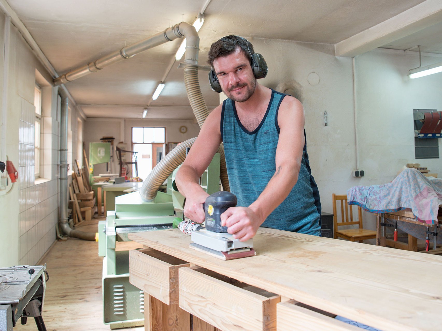 Holzwerkstatt: Ein Mann mit Gehörschutz arbeitet mit der Schleifmaschine
