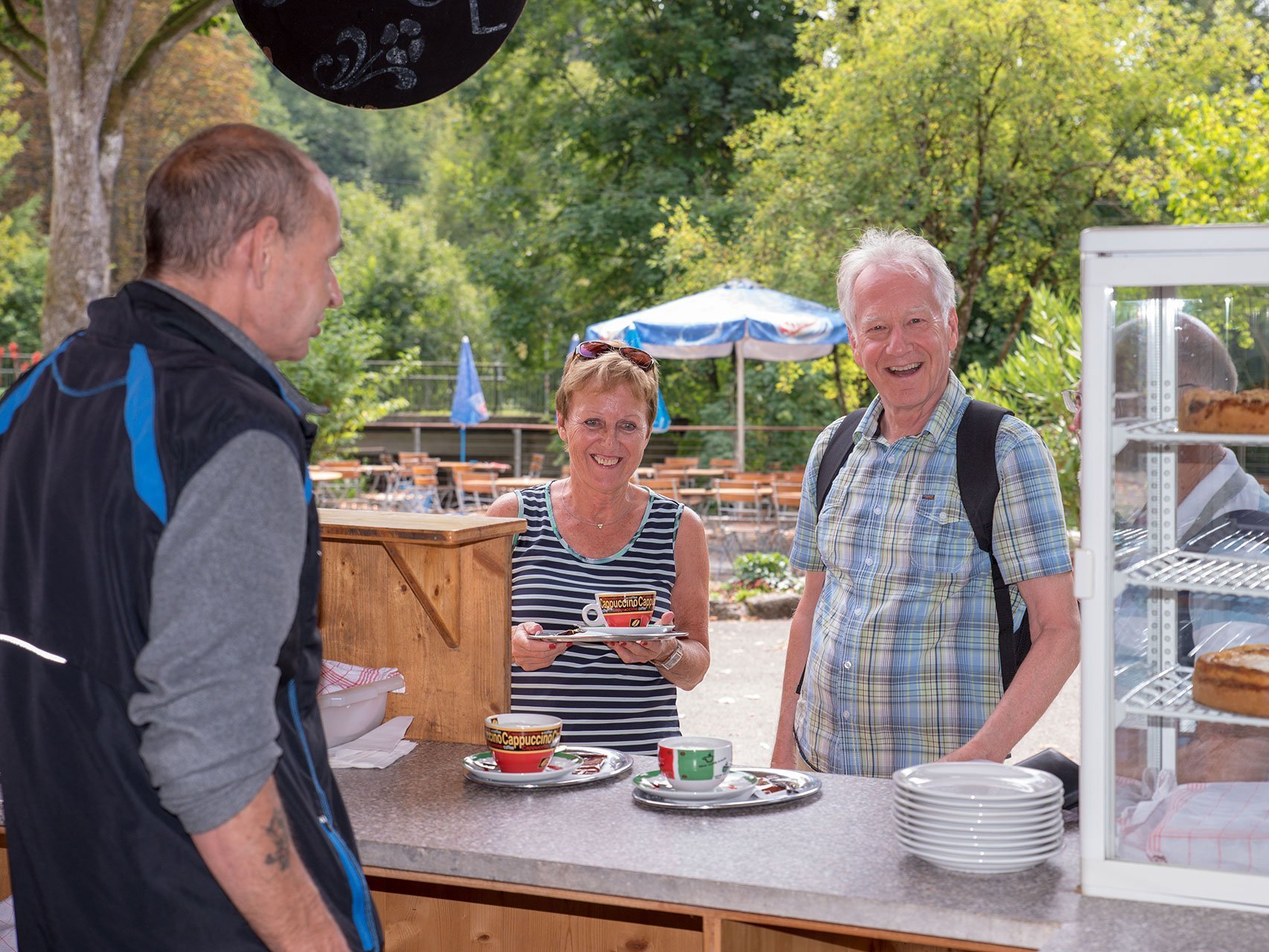 eine Frau und ein Mann stehen am Kaffee- und Kuchenverkauf - dort werden Sie von einem Mann bedient