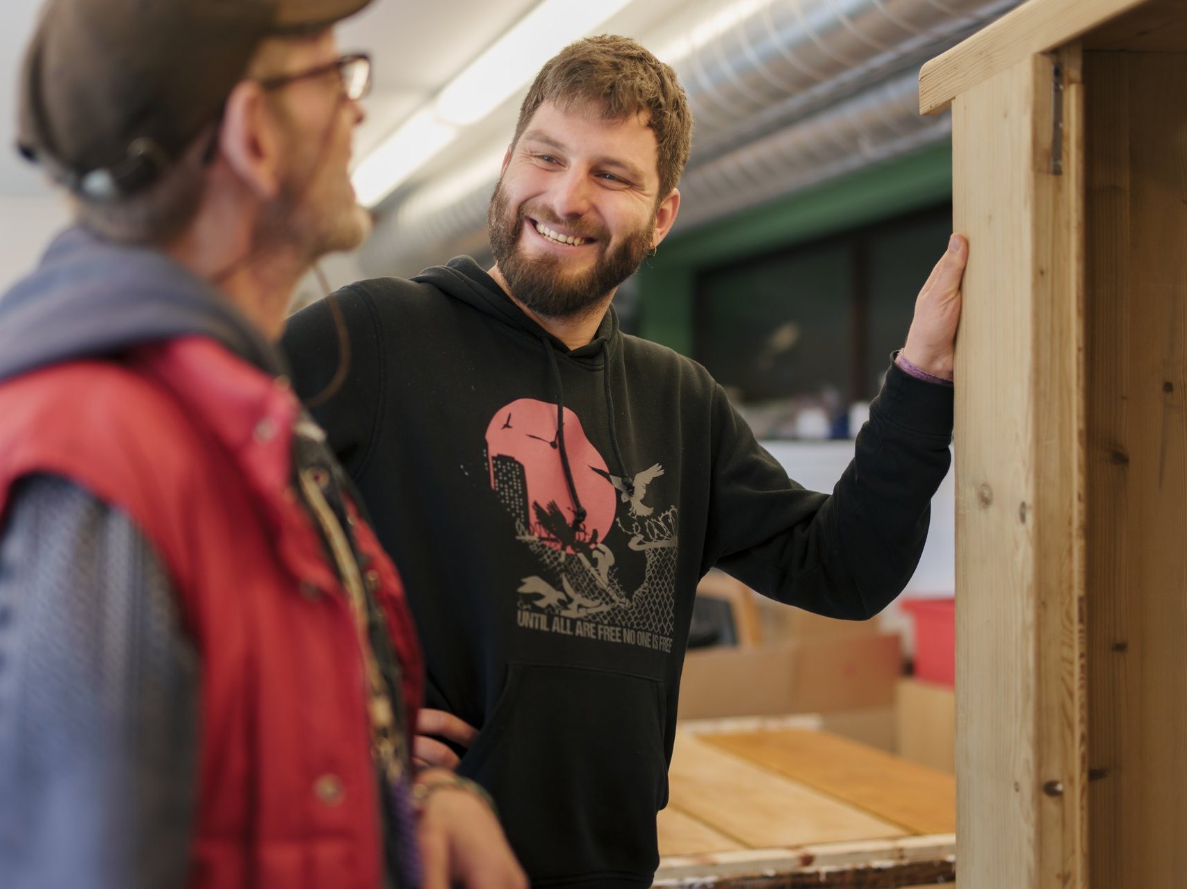 Zwei Menschen stehen in einer Schreinerwerkstatt und tauschen sich zu einem Werkstück aus.