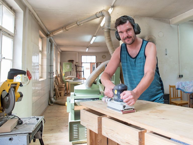 Holzwerkstatt: Ein Mann mit Gehörschutz arbeitet mit der Schleifmaschine