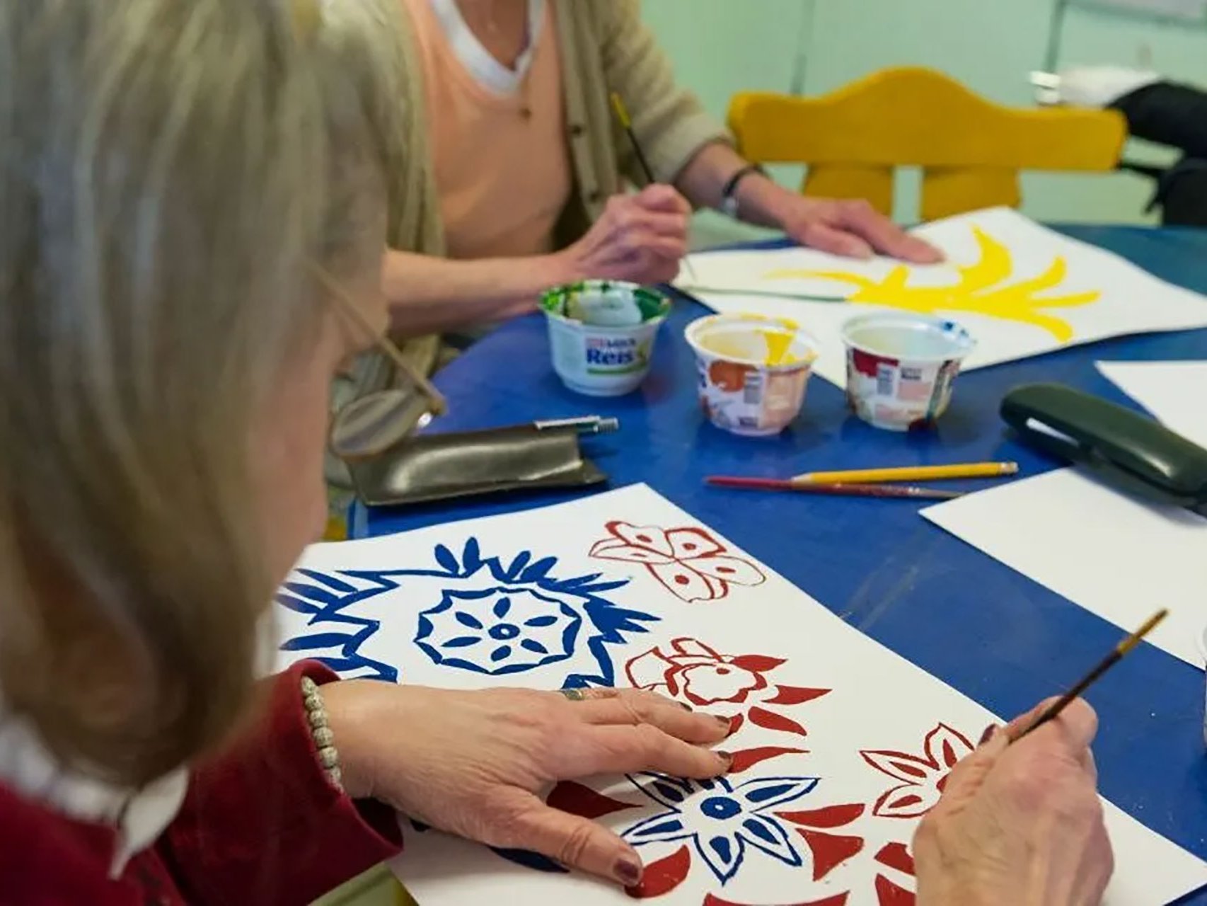 Nahaufnahme: zwei Frauen malen Blumenbilder auf weissem Papier an einem Tisch