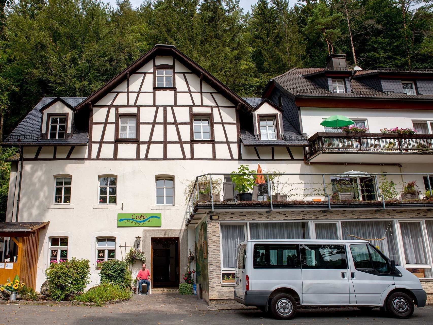 vor der Suchthilfe (Fachwerkhaus) steht ein Minibus - zu sehen ist auch ein Mann mit rotem T-Shirt, der neben der Eingangstür sitzt